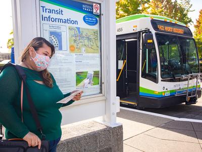 Woman standing in front of an intercity transit sign and bus reading a paper