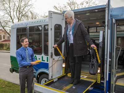 a Dial-A-Lift operator is assisting an elderly woman off the van